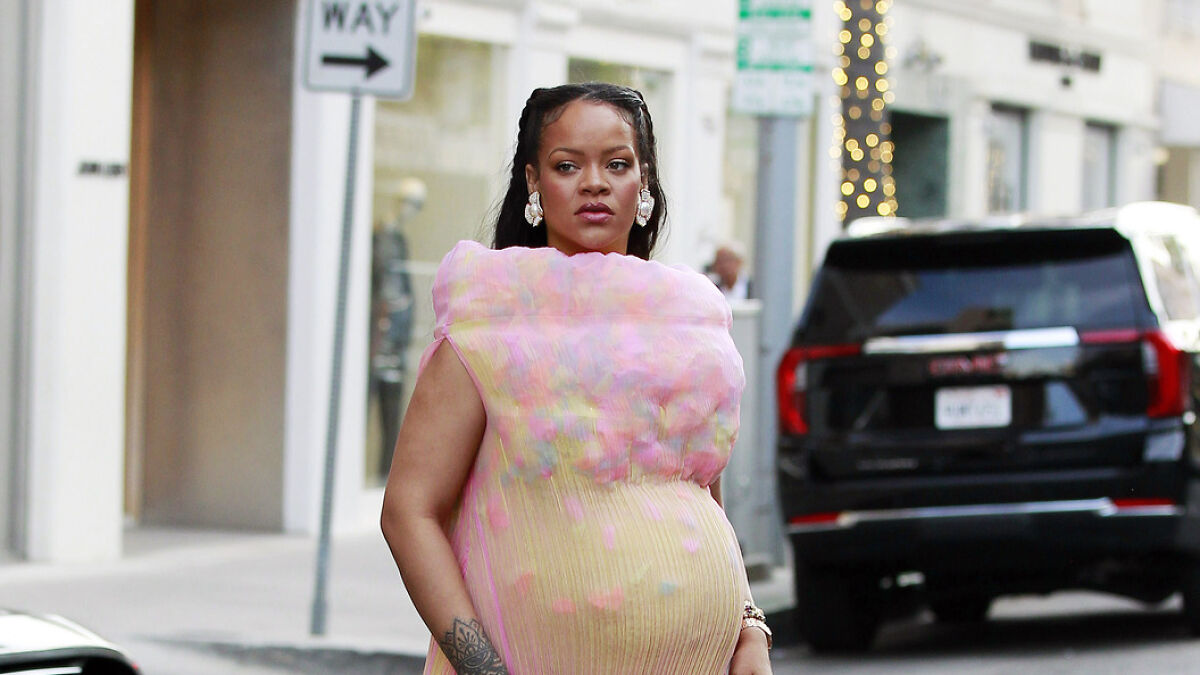 Rihanna wearing a colorful bloated maternity dress, walking outdoors with a serious expression and stylish accessories.