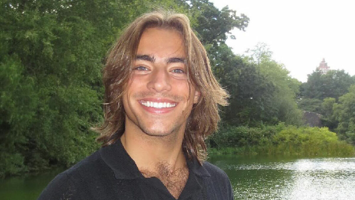 Young man with shoulder-length hair smiling outdoors near greenery and water, related to Chase Filandro news.