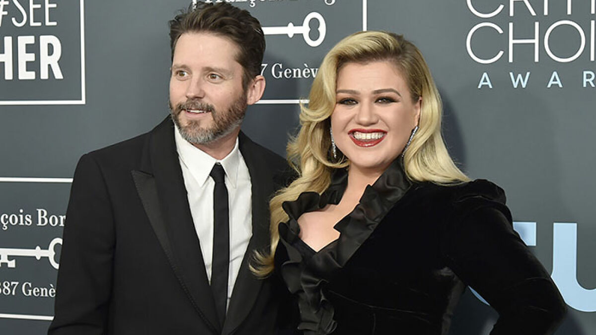 Kelly Clarkson smiling in a black dress with a man in a black suit at a Critics Choice Awards event.