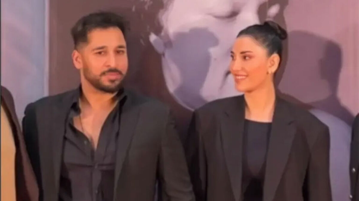 Intoxicated man and supermodel wife in black outfits, with the wife smiling while defending his pain publicly.