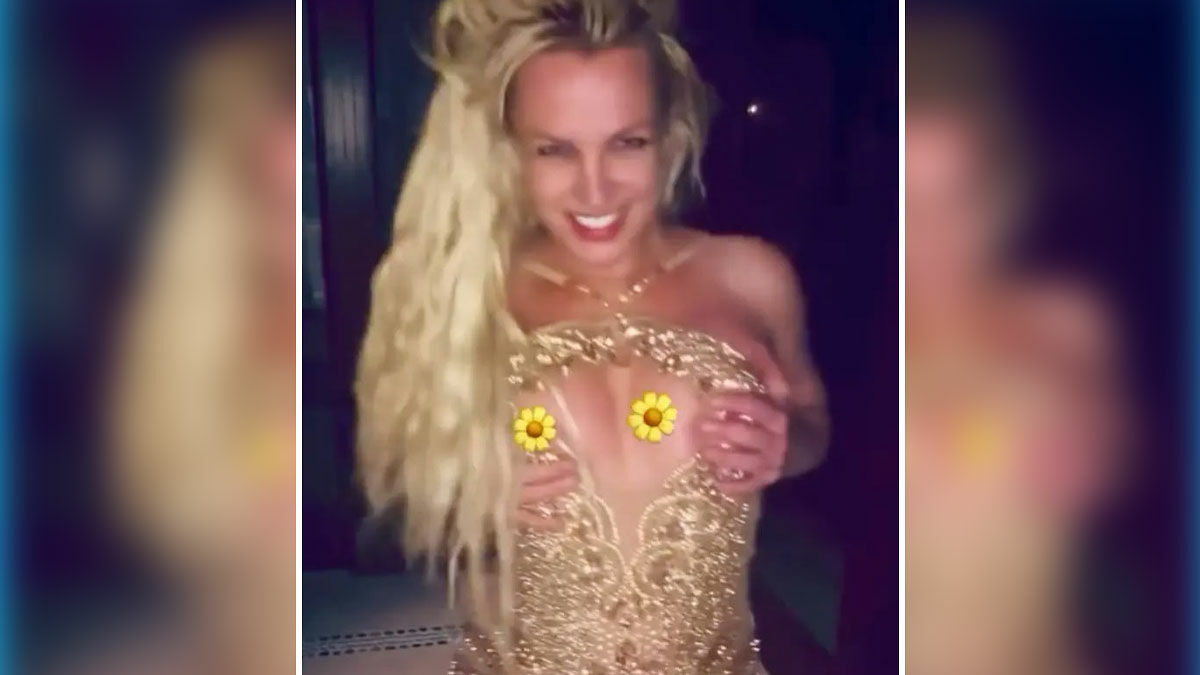 Britney Spears in a gold minidress during a daring dance moment causing a wardrobe nip slip, smiling at the camera.