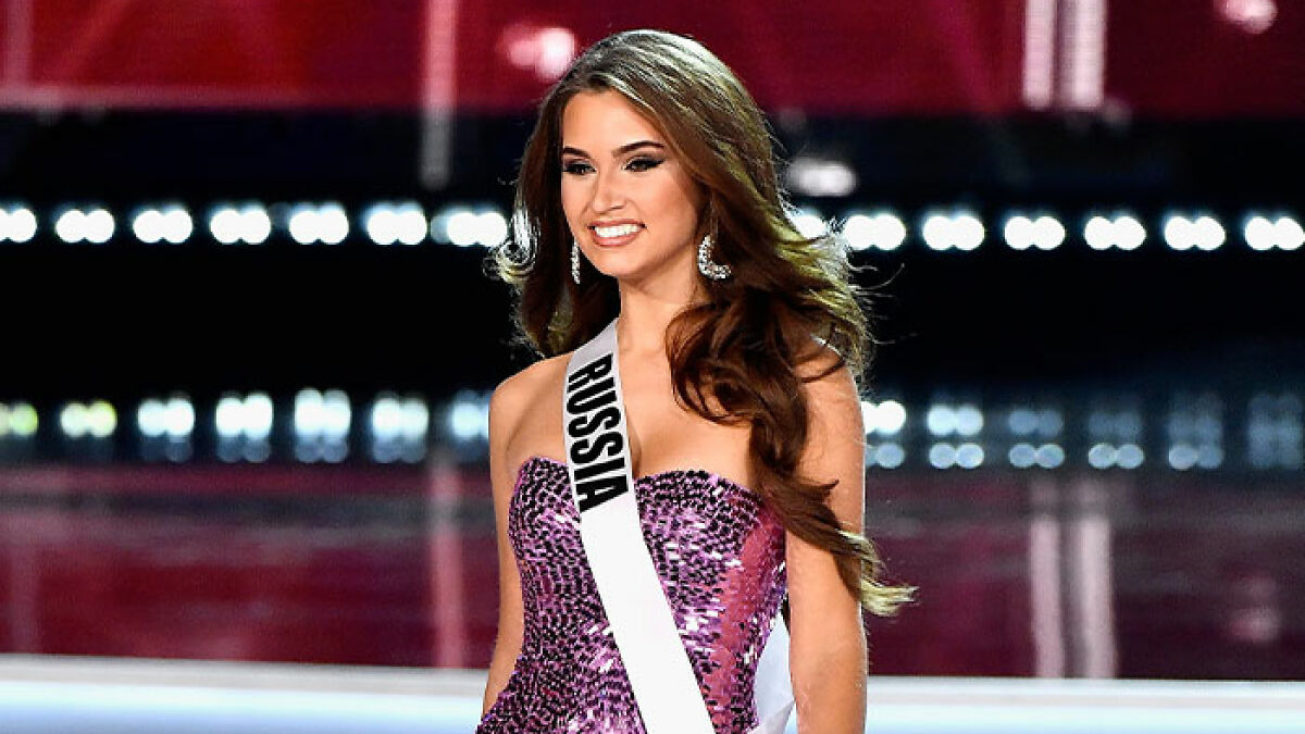 Former Miss Universe contestant from Russia smiling in a purple gown and sash on stage during a beauty pageant.