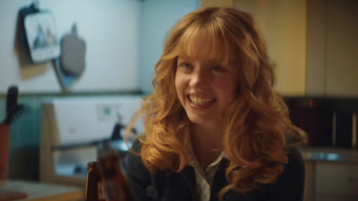 Sydney Sweeney smiling with curly hair in a kitchen scene from her new movie amid box office flop and American Eagle backlash.