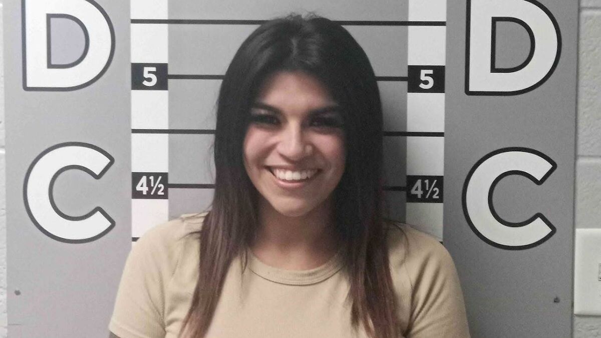 Woman smiling in a mugshot photo after destroying ex's car by pouring salt in engine and glitter in AC