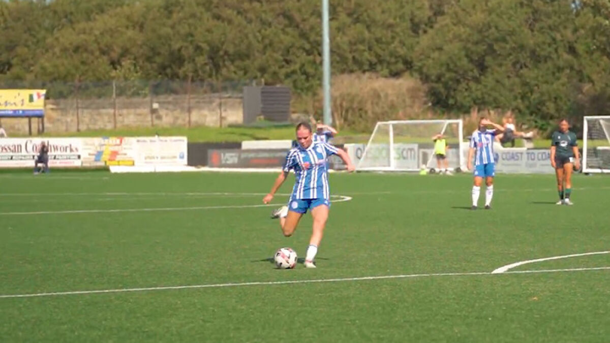 16YO footballer in blue and white uniform kicking ball on field during a daytime match with players in background