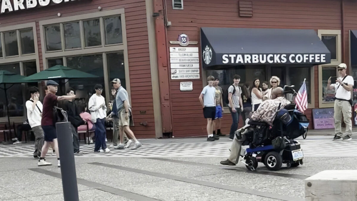 Man in a wheelchair outside Starbucks Coffee with people walking nearby, highlighting disabled veteran and proof of service.