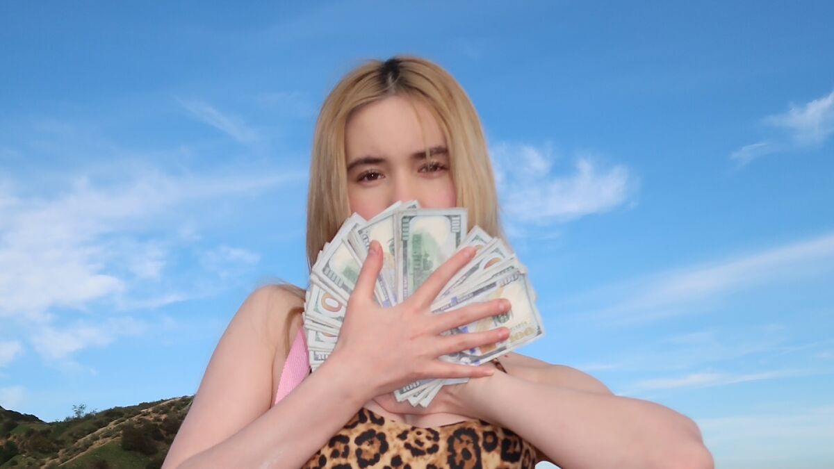Adult star holding cash outdoors against blue sky encouraging women to join OF over 9 to 5 jobs.