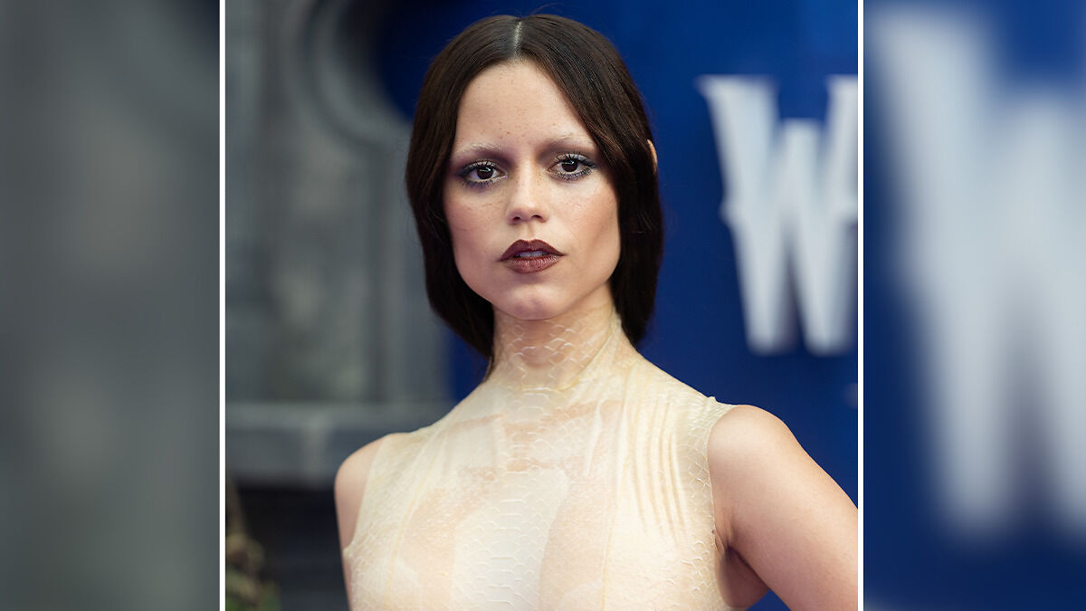 Young woman with tired girl beauty trend makeup, dark lipstick, and subtle eye shadows posing at an event.