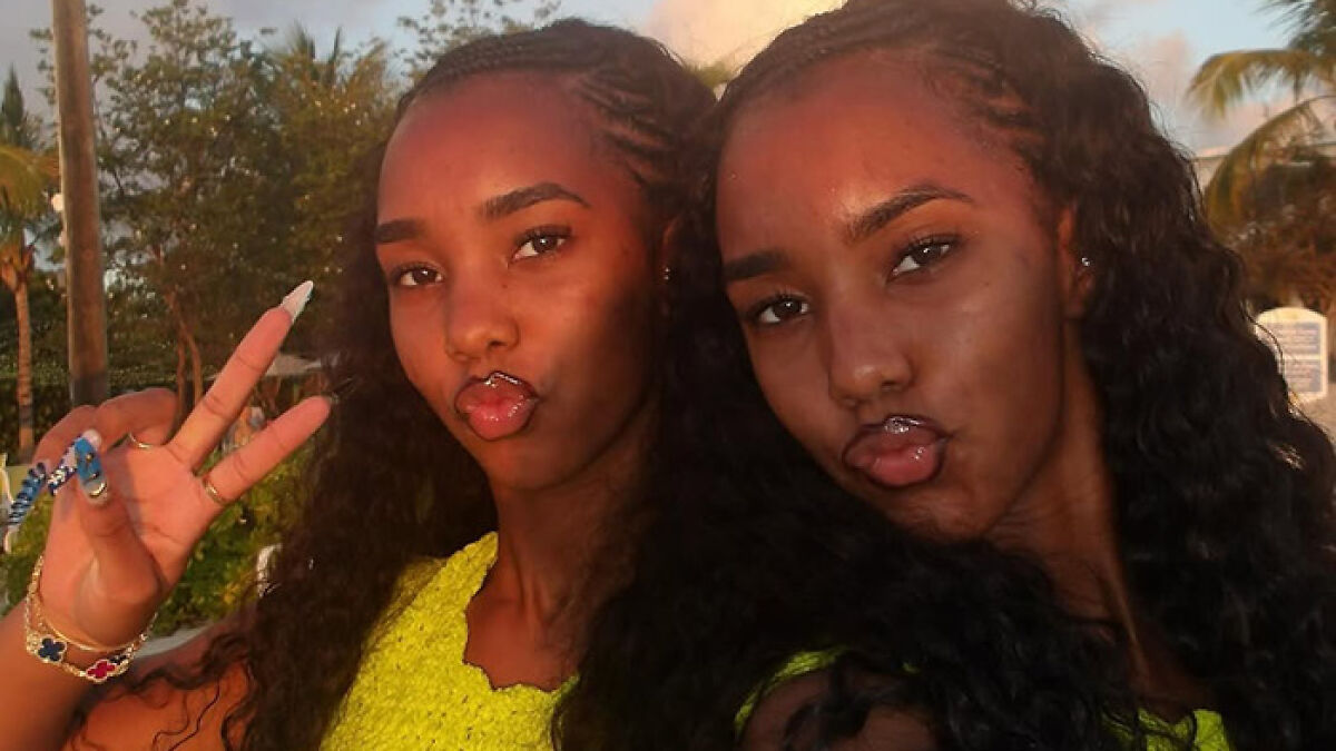 Sean Diddy's twin daughters posing outdoors with peace signs and playful expressions during golden hour in a tropical setting.