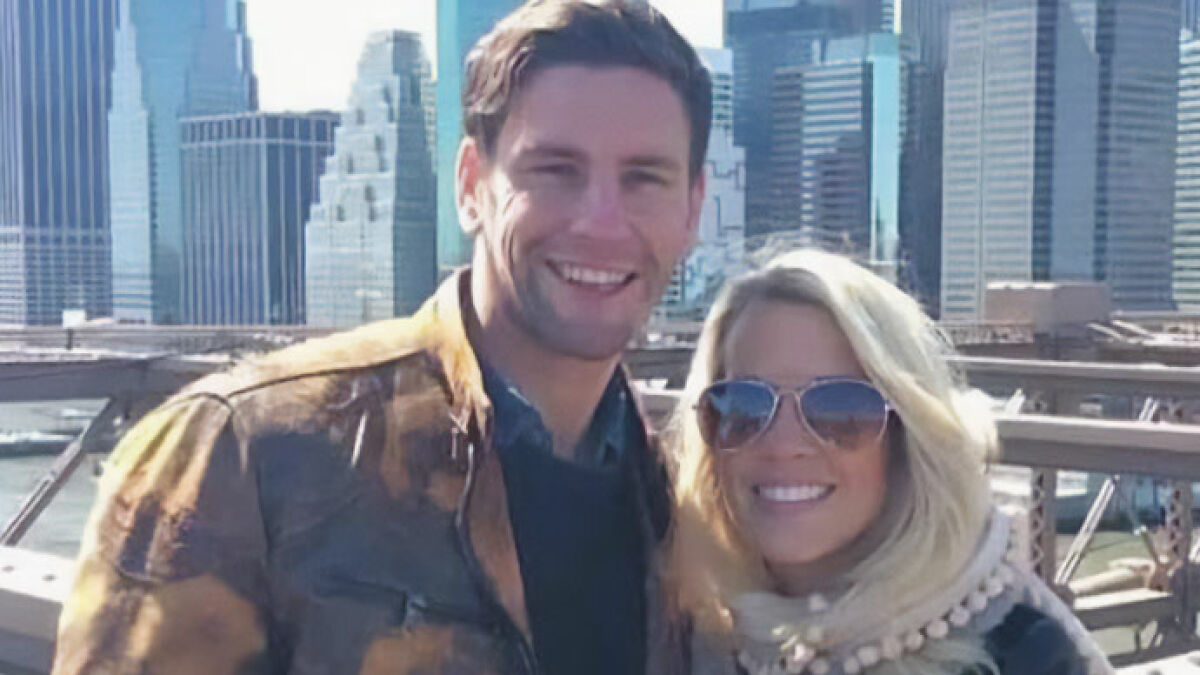 Couple accused of squatting in abandoned million-dollar house posing outdoors with city skyline in background.