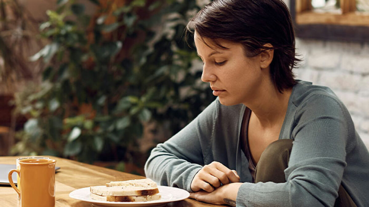 Woman sitting at table appearing in pain, reflecting on her rare disorder after doctors dismissed her persistent pain.