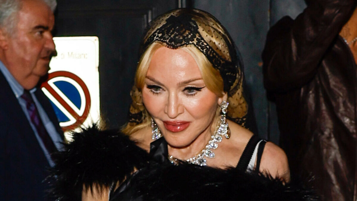 Celebrity seen without makeup or professional lighting, wearing a vintage-style headscarf and statement jewelry at an event.