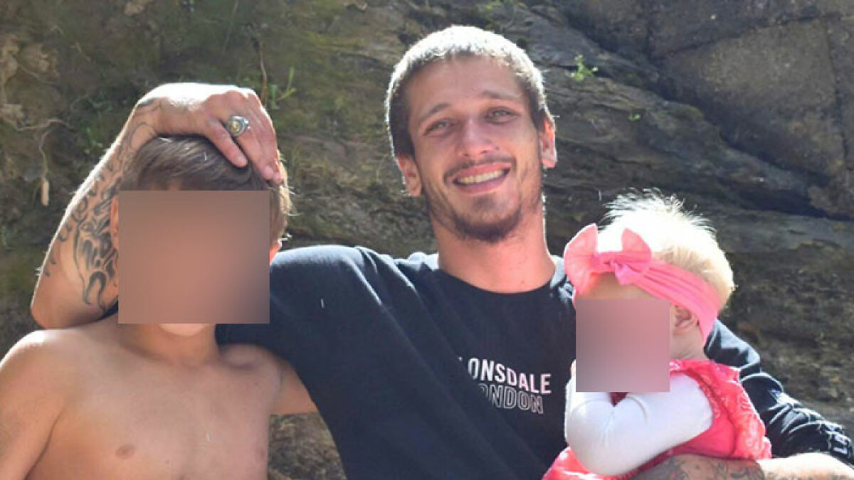 Man with tattoos and beard smiling outdoors with two young children, related to dad losing life after being buried alive digging sand.