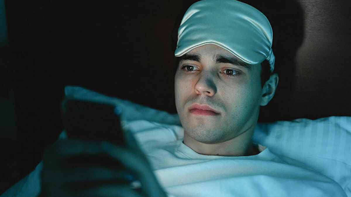 Young man who hasn't slept in 2 years lying awake in bed at night, looking at phone with tired eyes.