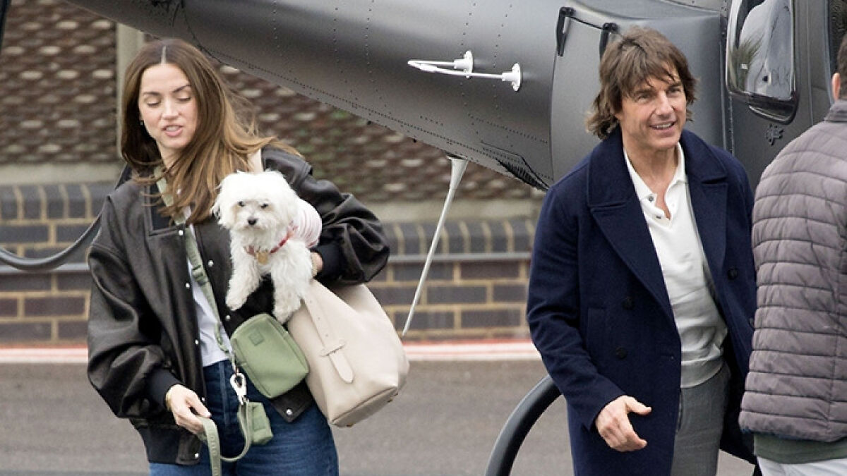 Tom Cruise and Ana de Armas walking near a helicopter with a small white dog in casual outdoor attire