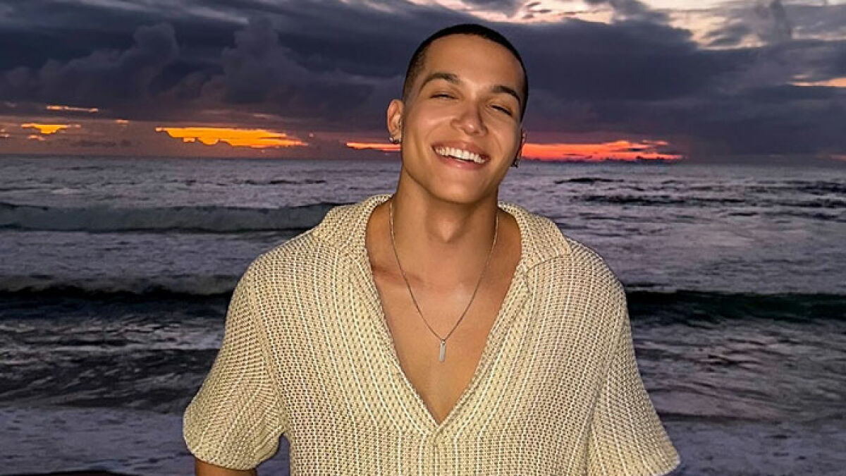 Young man smiling at ocean during sunset, related to tragedy and mystery in luxury hotel involving model found dead.