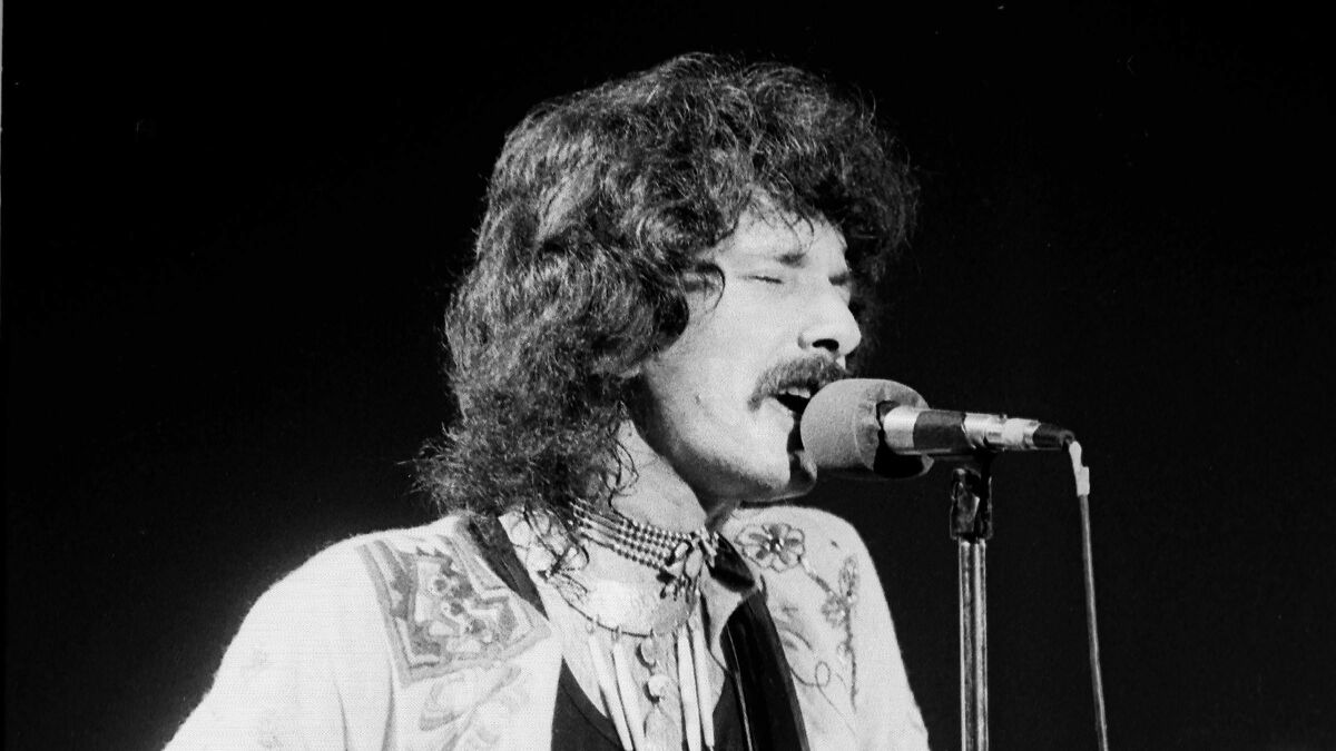 Male celebrity singing passionately into a microphone during a live performance in a black and white image.