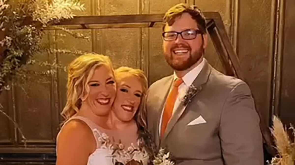 Hensel twins smiling with a man in a suit at a wedding, sparking speculation about motherhood and marriage.