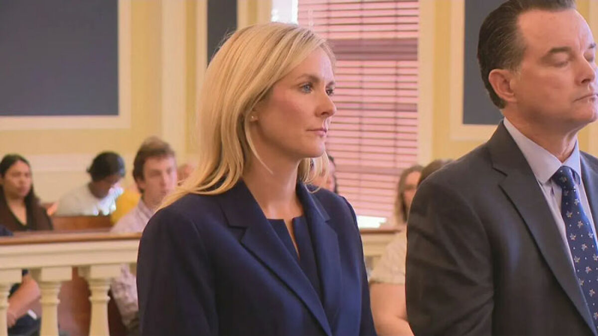Prosecutor standing in courtroom during hearing, appearing serious as courtroom audience observes the proceedings.