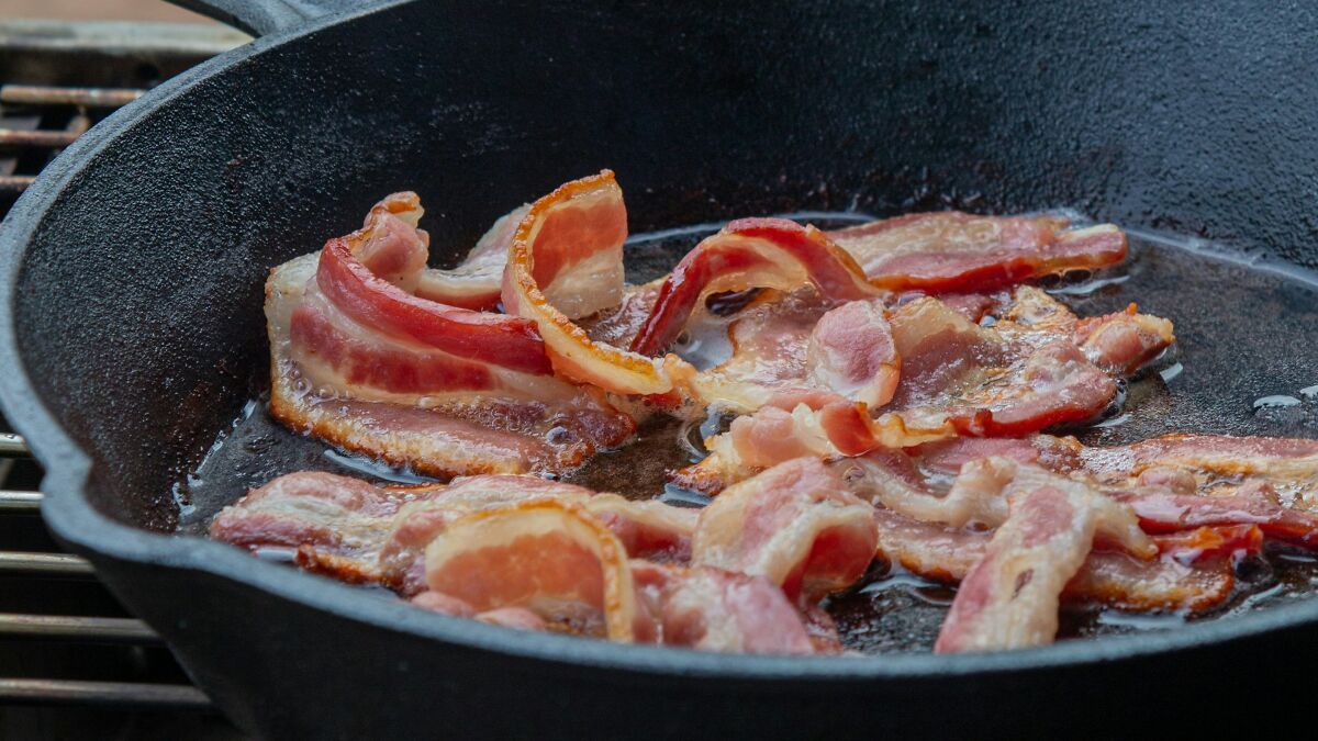 Sizzling bacon cooking in a cast iron skillet, illustrating risks related to pork worms from common bacon habits