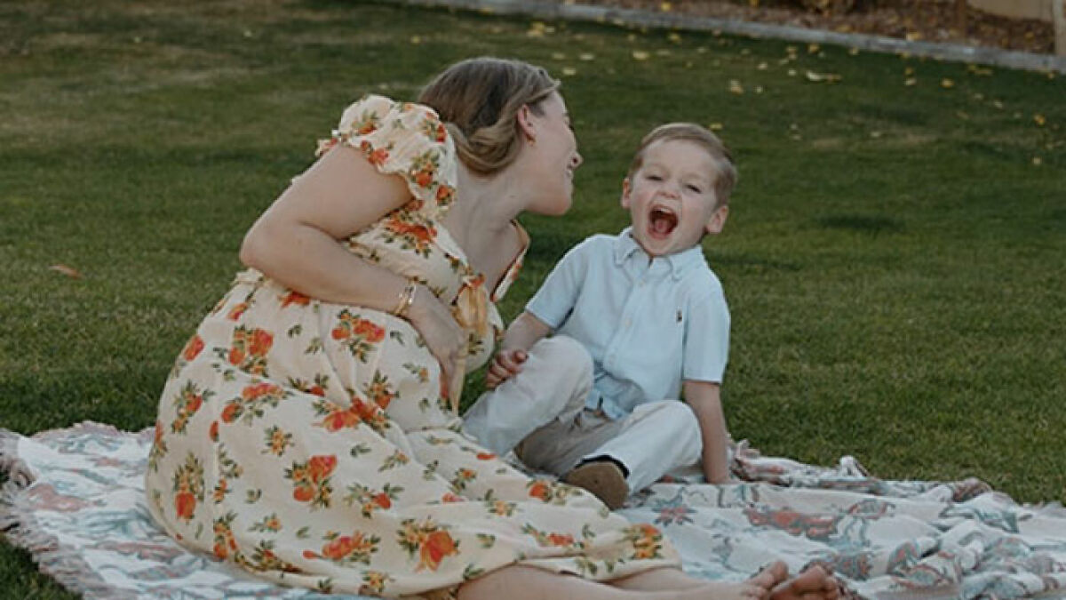Mother and young son sitting on blanket in grass, illustrating momfluencer after tragic drowning incident.