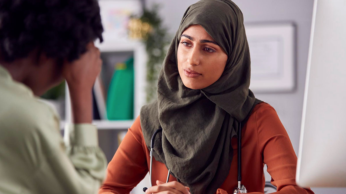 Muslim woman in hijab listening attentively to coworker in office, addressing coworker misgenders on religion issue.