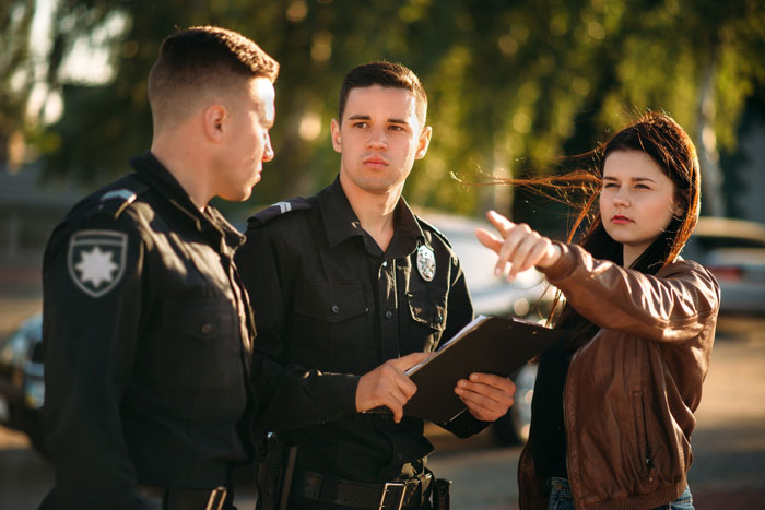 Woman pointing while talking to two police officers outside, concerned about nephew’s safety and controlling brother issues. Woman pointing while talking to two police officers outside, concerned about nephew’s safety and controlling brother issues.