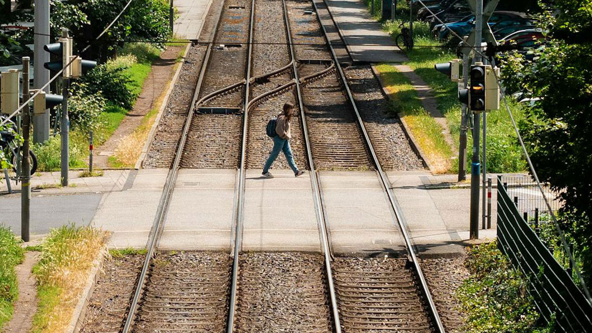 Person crossing train tracks at a railway crossing, illustrating people surviving crazy situations safely.