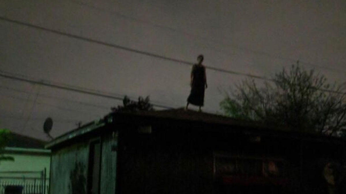 Silhouetted figure standing on dark rooftop at night in a creepy and unsettling moment captured outdoors.