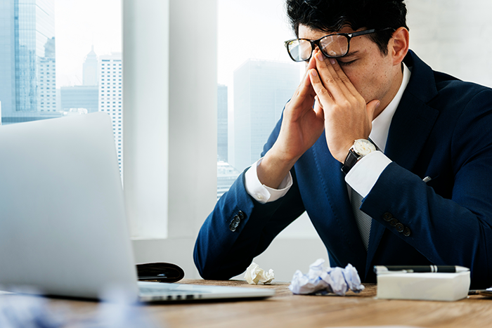 Worker in office looking stressed and disciplined, wearing glasses and suit, with crumpled papers on desk near laptop. Worker in office looking stressed and disciplined, wearing glasses and suit, with crumpled papers on desk near laptop.
