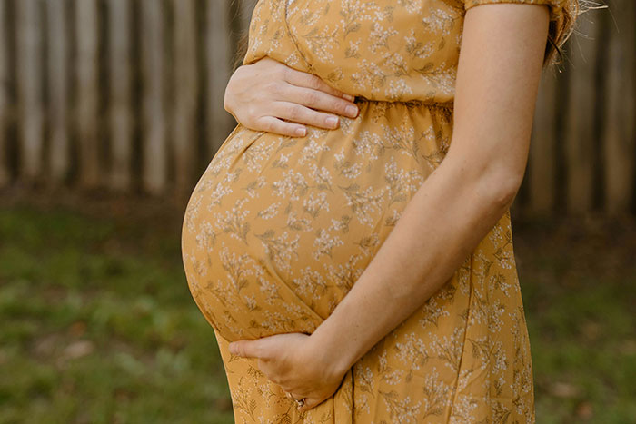 Pregnant woman in a yellow floral dress holding belly outdoors, representing dad’s difficult decision to call CPS on teen daughter. Pregnant woman in a yellow floral dress holding belly outdoors, representing dad’s difficult decision to call CPS on teen daughter.
