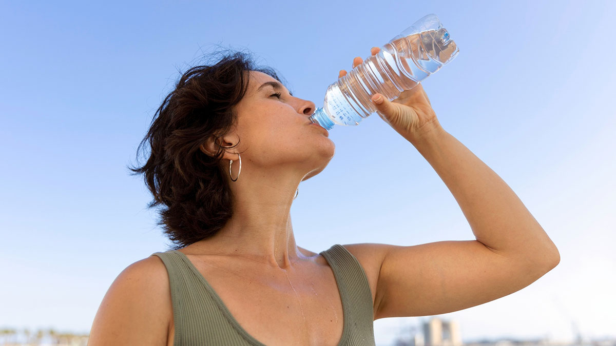 Woman drinking water from plastic bottle outdoors, illustrating aspects of modern life close to breaking down.