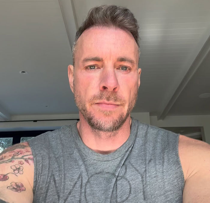 Dax Shepard in a sleeveless shirt, showing tattoos, appearing relaxed in a well-lit indoor setting. Dax Shepard in a sleeveless shirt, showing tattoos, appearing relaxed in a well-lit indoor setting.