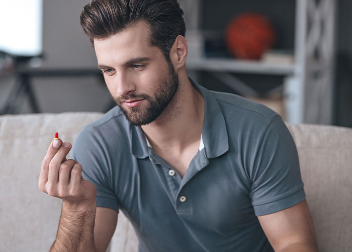 Man sitting on couch looking thoughtfully at a pill, reflecting on disgustingly shocking things about friends discovered