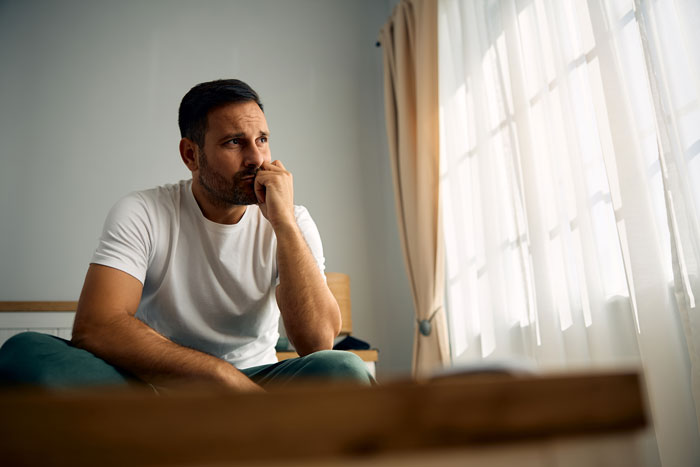 Man sitting pensively by a window, portraying the emotional impact of in-laws' concerns about weight and divorce. Man sitting pensively by a window, portraying the emotional impact of in-laws' concerns about weight and divorce.