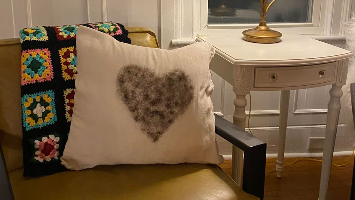 Pillow with a heart-shaped DIY disaster made of felted wool on a chair next to a white vintage side table.