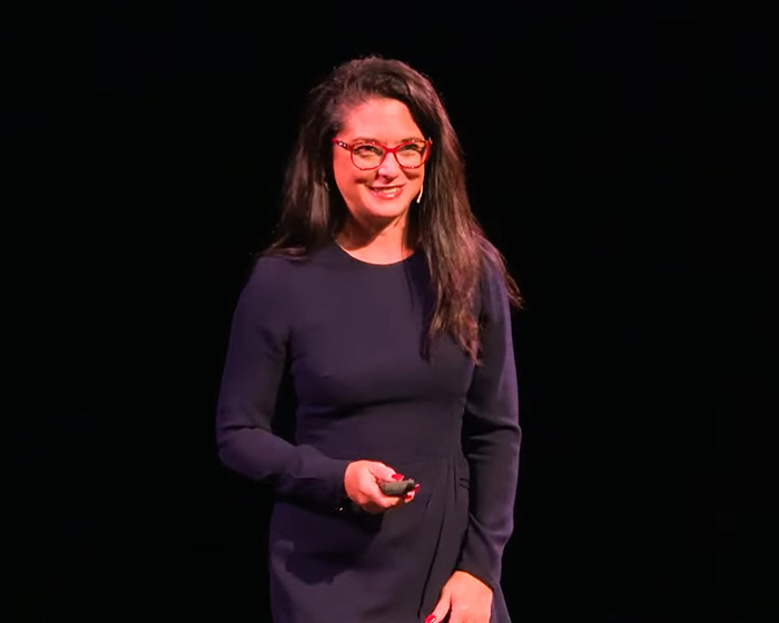 Woman wearing glasses and a dark dress speaking onstage about the doctor reveals 11 push-ups challenge for women. Woman wearing glasses and a dark dress speaking onstage about the doctor reveals 11 push-ups challenge for women.
