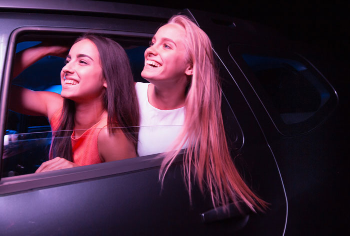 Two young women smiling and leaning out of a car window, capturing a moment related to parking spot revenge. Two young women smiling and leaning out of a car window, capturing a moment related to parking spot revenge.