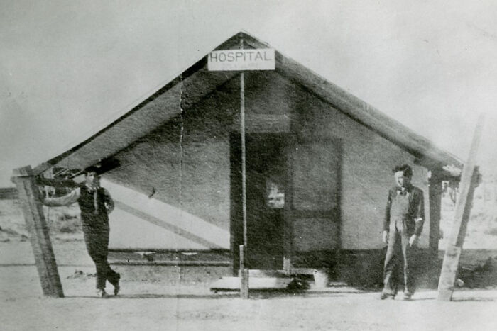 Two men standing outside a small makeshift hospital in early 20th century historic Vegas desert setting.