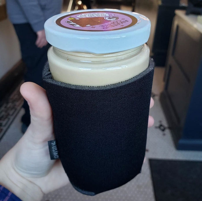 Hand holding a unique drink in a glass jar wrapped with a black sleeve at creative bars and restaurants worldwide.