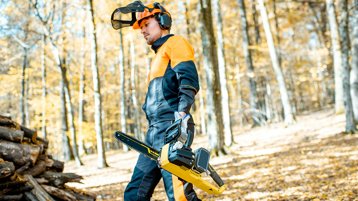 Lumberjack in safety gear carrying chainsaw in forest, illustrating real-life horror stories from the emergency room.