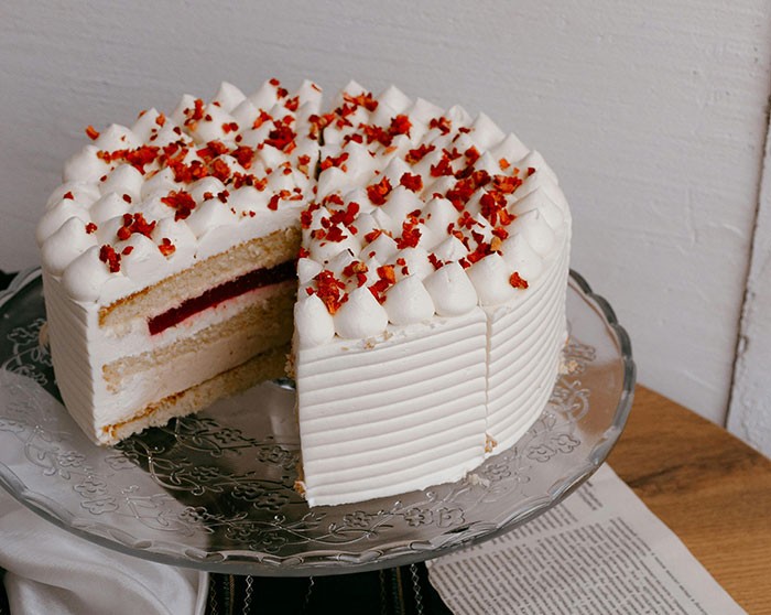 White layered cake with cream and red sprinkles on a glass stand, related to woman threatening bakery over refund dispute.