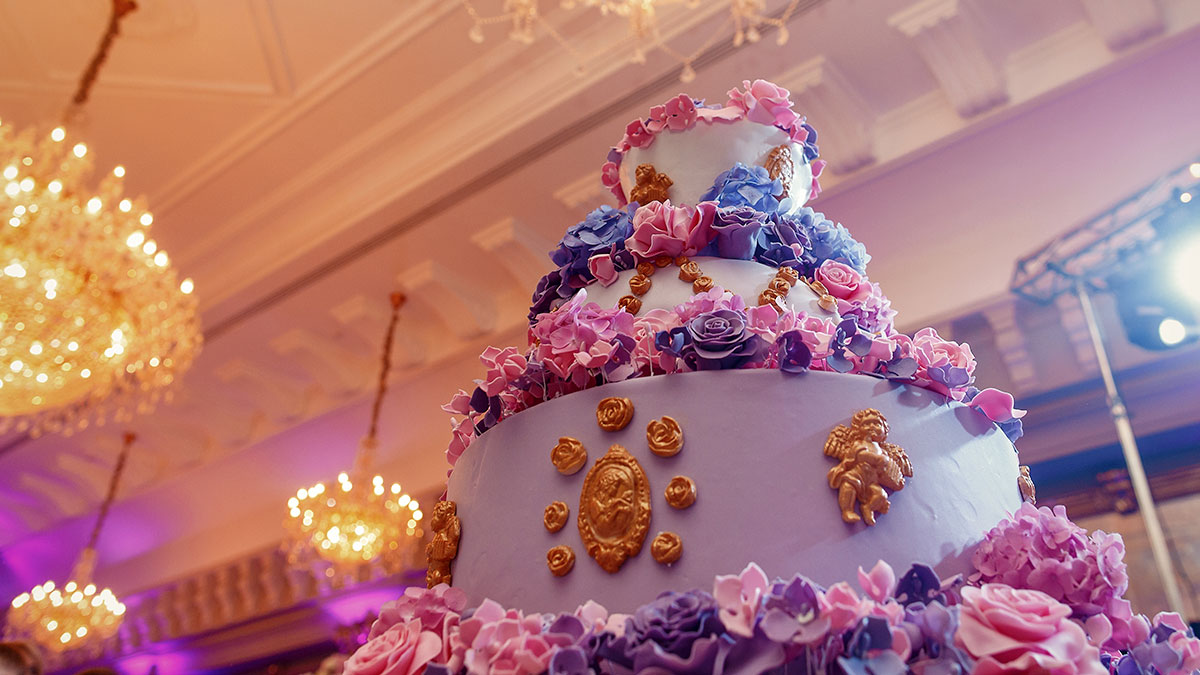 Multi-tiered decorated cake with flowers and cherubs in a banquet hall, related to bakery and social media roasting keywords.