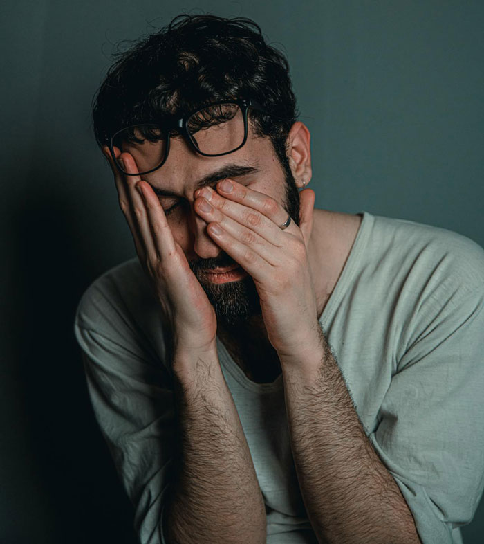 Man with glasses and beard, looking stressed and frustrated while covering his face with his hands indoors. Man with glasses and beard, looking stressed and frustrated while covering his face with his hands indoors.