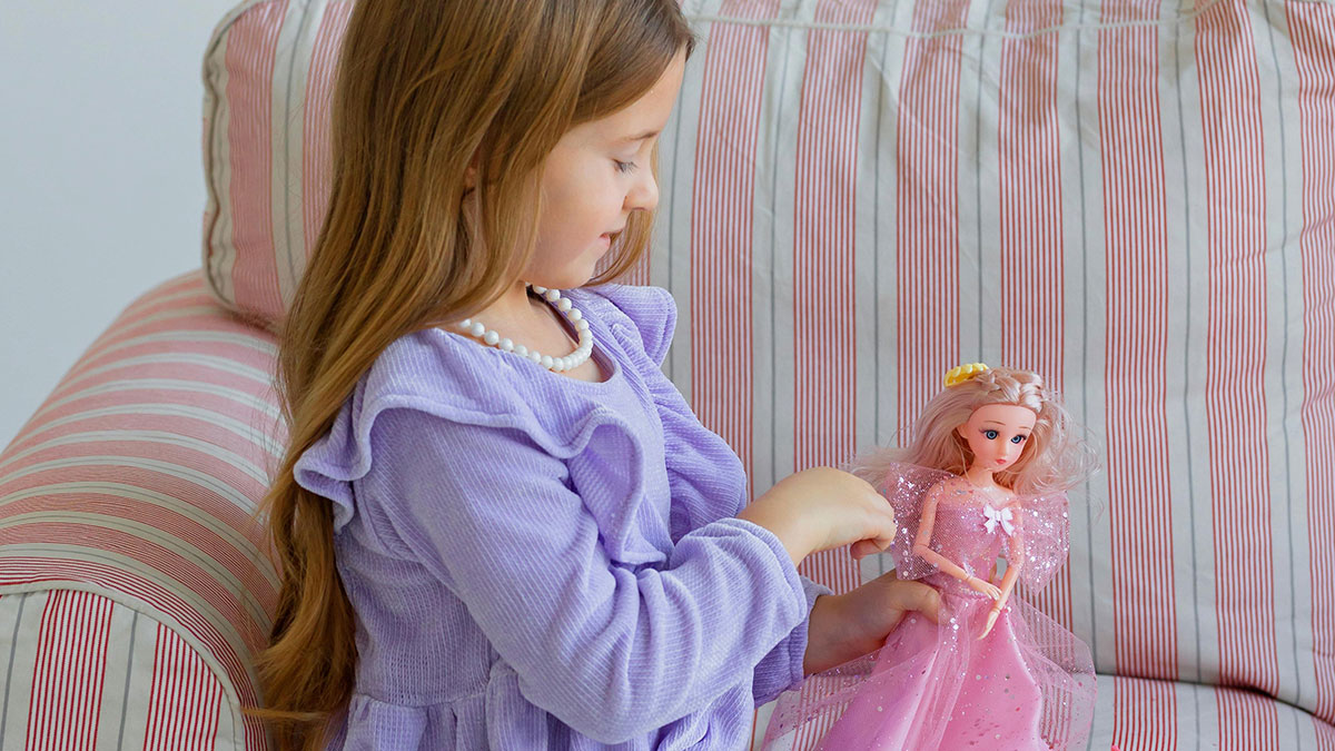 Young girl in a purple dress holding a collector doll on a striped couch indoors, focused on the doll's details.