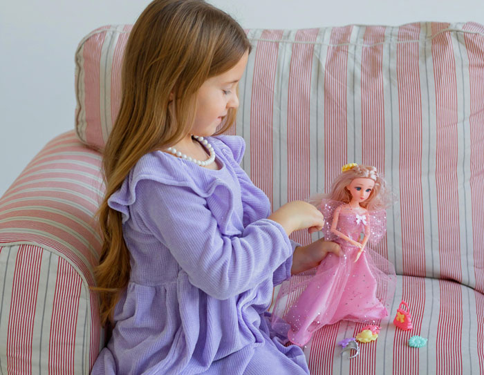 Young girl in a purple dress playing with a collector doll on a striped sofa, highlighting woman catching guest sneaking. Young girl in a purple dress playing with a collector doll on a striped sofa, highlighting woman catching guest sneaking.