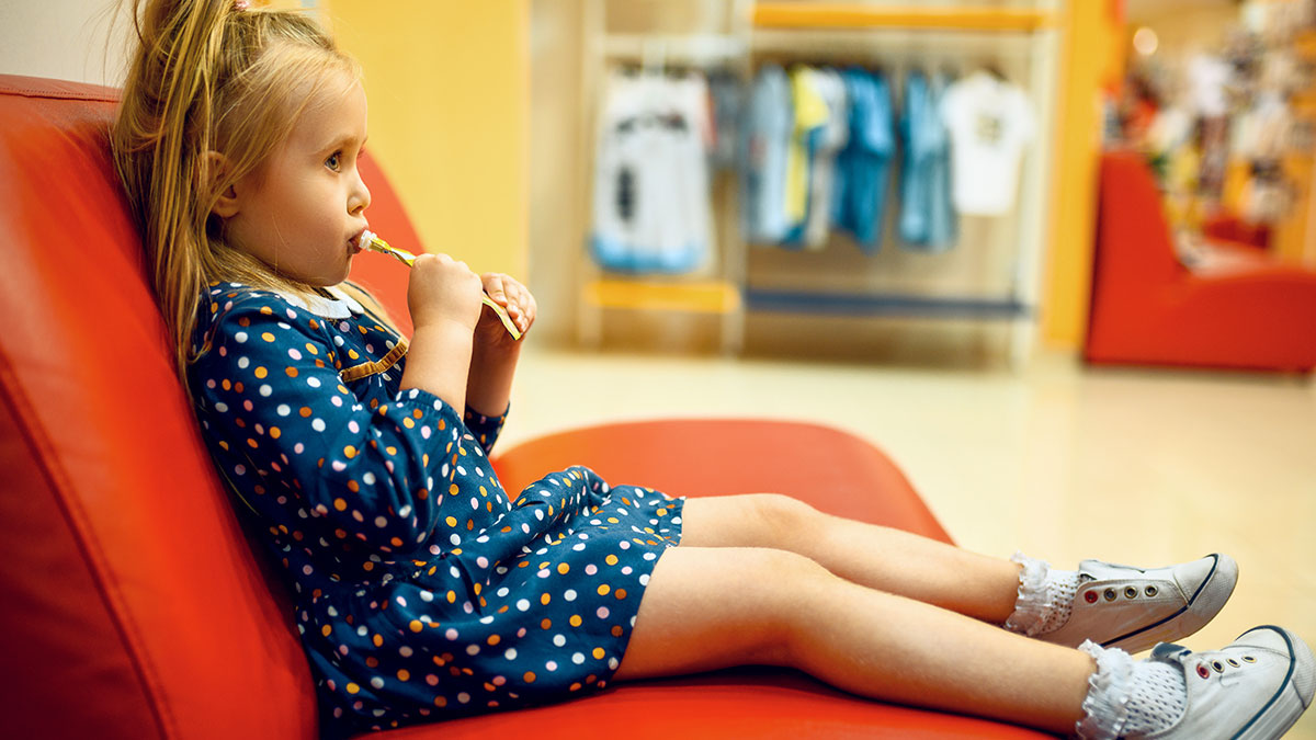 Two-year-old niece sitting on a red couch, waiting during a doctor appointment with her uncle.
