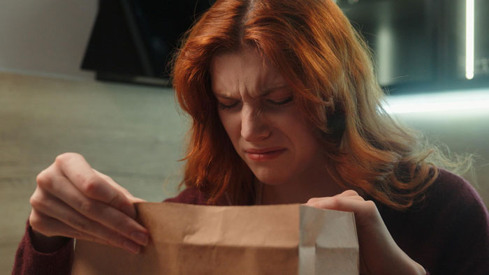 A red-haired woman displaying a pained expression while opening a brown paper bag, reflecting betrayal and revenge feelings. A red-haired woman displaying a pained expression while opening a brown paper bag, reflecting betrayal and revenge feelings.