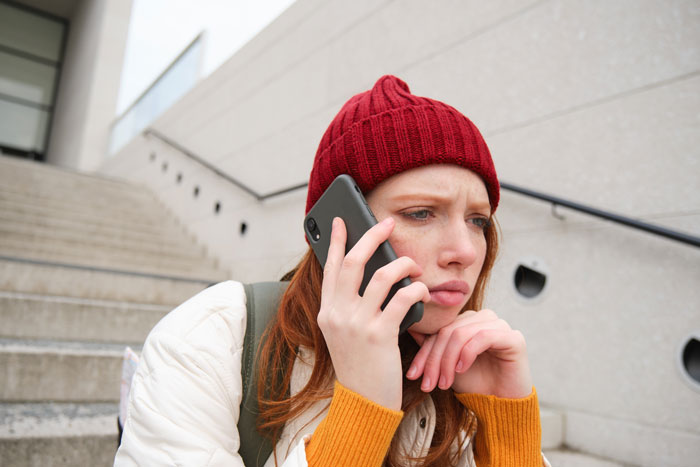 Young woman in red beanie looking troubled while talking on phone, reflecting feelings of betrayal and revenge. Young woman in red beanie looking troubled while talking on phone, reflecting feelings of betrayal and revenge.