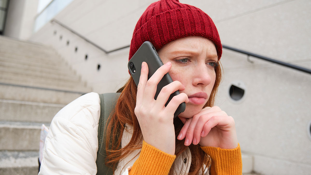Young woman in a red beanie looking upset while talking on the phone, reflecting feelings of betrayal and revenge.
